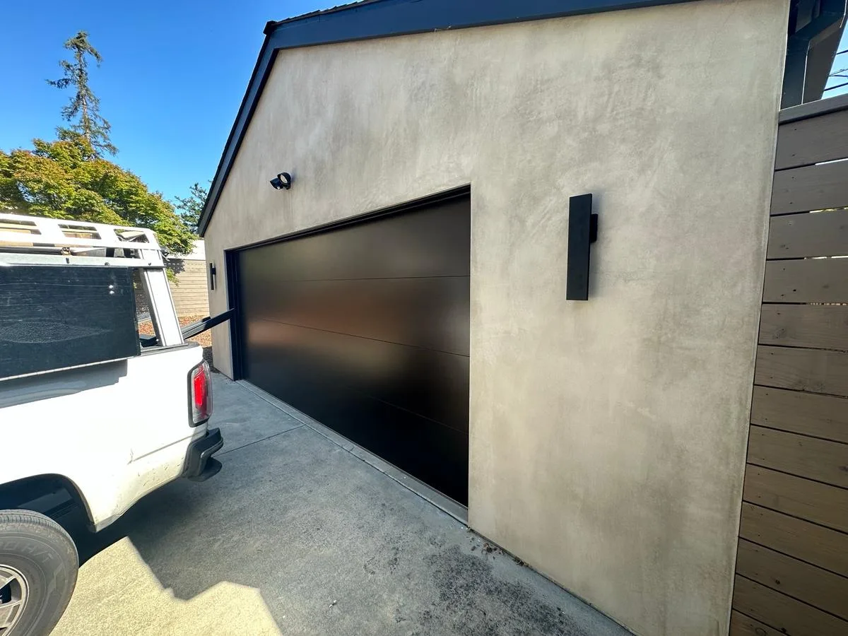 Black modern flush panel garage door on stucco building