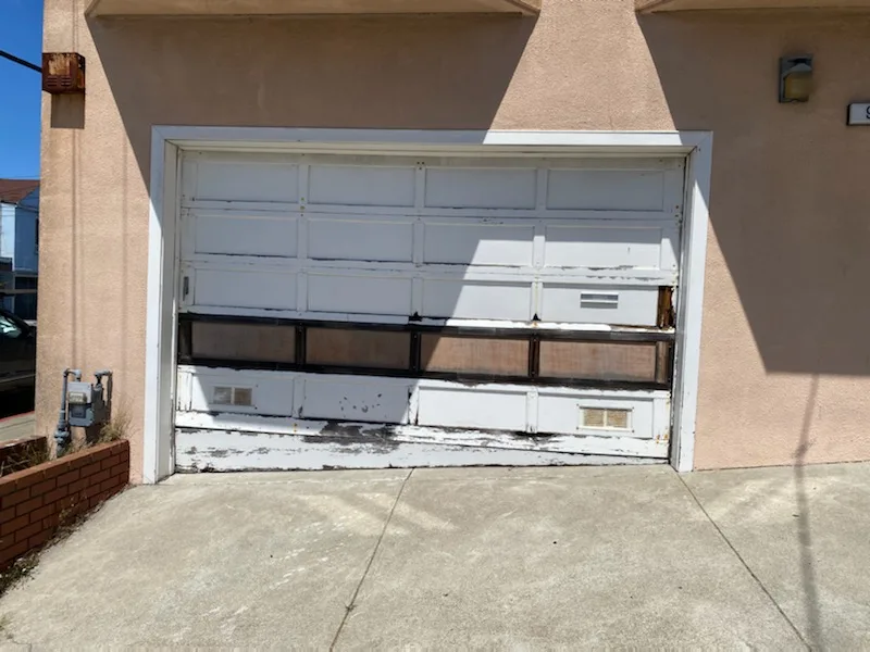 Old damaged residential garage door with broken panels and peeling paint